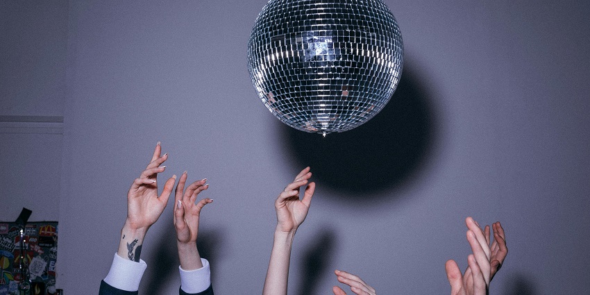 Hands in the air of people dancing below a hanging shining disco ball casting shadow, displaying Mauritius nightlife.