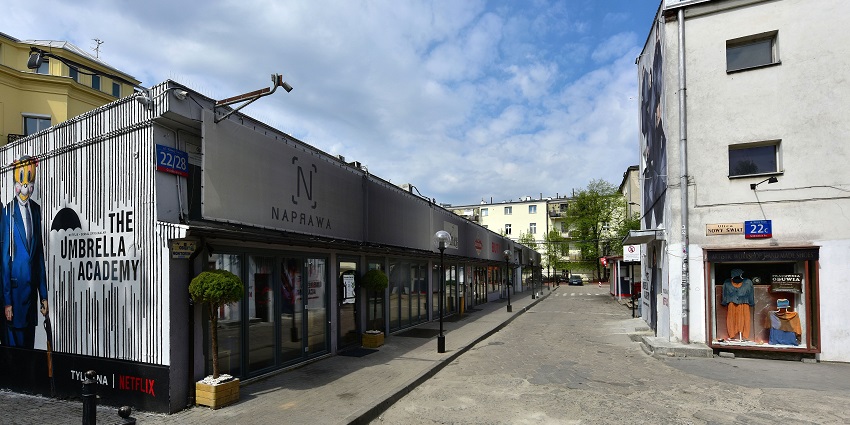 Pawilony Nowy Świat with street side lamps and cars parked outside the buildings.