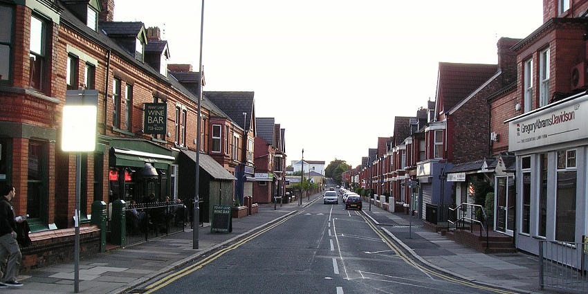 An image of the view down Penny Lane, lined with brick buildings, shops and restaurants in Liverpool.