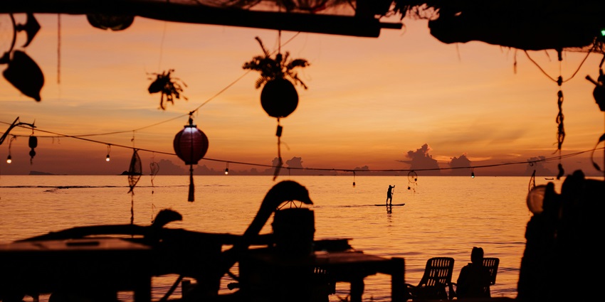 Beach bar in the evening with orange sky during sunset with silhouettes of hanging lamps