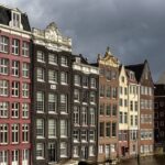 Colourful canal houses at golden hour in Damrak avenue in Amsterdam.