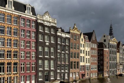 Colourful canal houses at golden hour in Damrak avenue in Amsterdam.