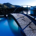 An image of a blue and black swimming pool near a brown wooden dock during daytime.