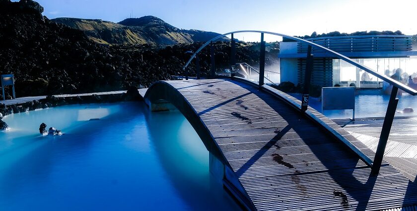 An image of a blue and black swimming pool near a brown wooden dock during daytime.