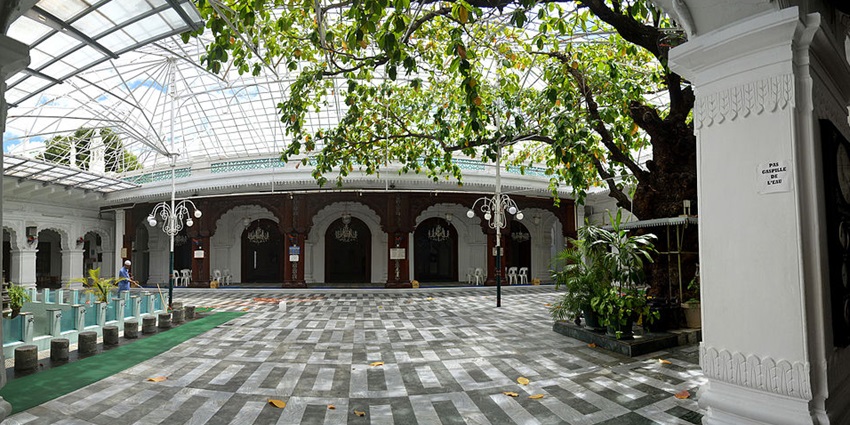 Inside the jummah masjid in Port Louis with a tree inside and a man in the complex area.