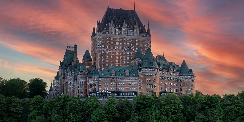 Tall Chateau Frontenac Hotel in Quebec with modern architecture, surrounded by greenery.