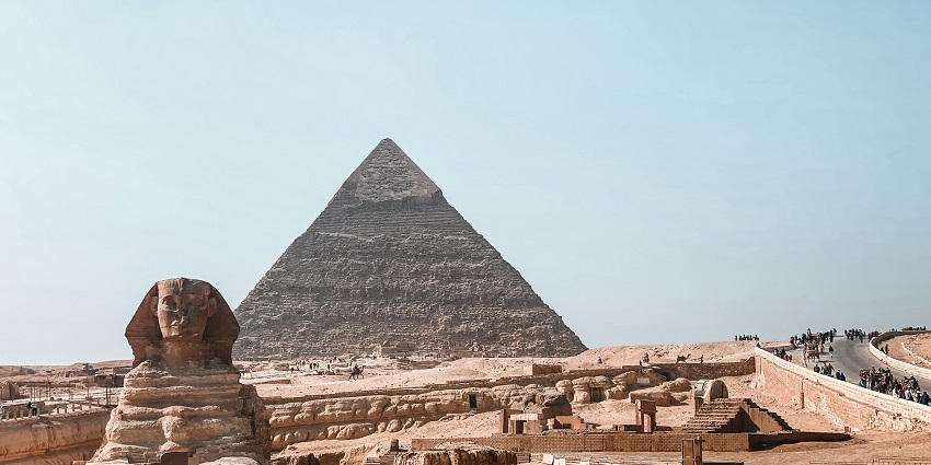 The Sun is setting behind the Pyramids of Giza, leaving the sky slightly orange and tranquil.