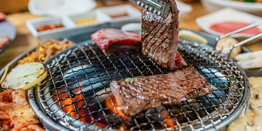 Grilled meat with bones placed on a dark surface and fresh green leaves next to it