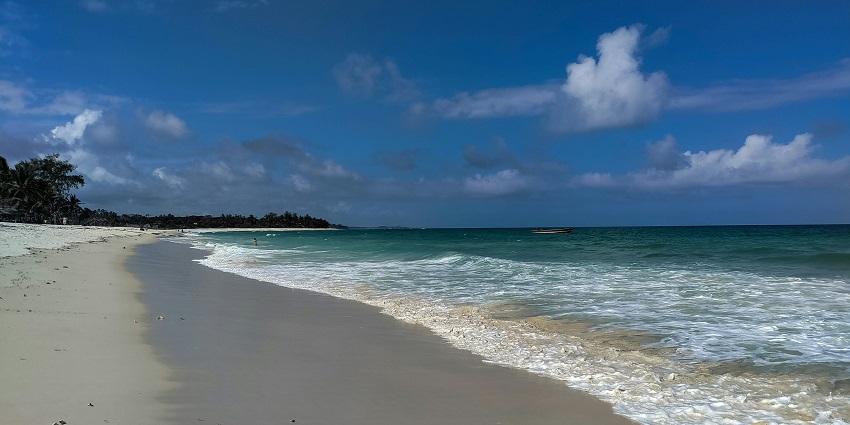 Turquoise water from the sea is crashing on Diani Beach in Kenya under the blue sky.
