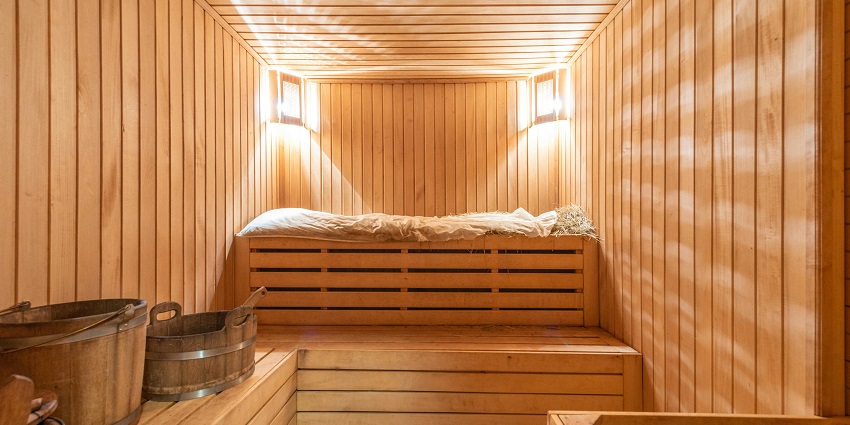 Inside a Sauna with wooden walls illuminated by two lamps and buckets placed on seats
