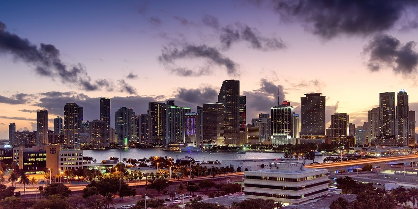 An image of the Miami skyline at sunset with vibrant colours in the sky and calm water below.