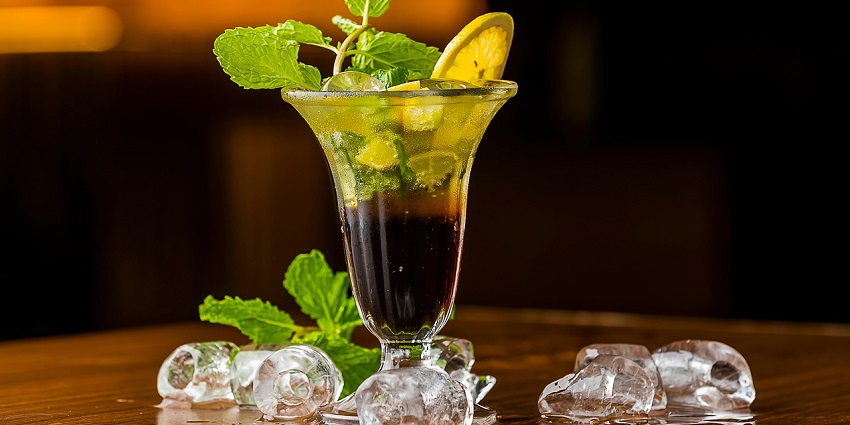 Image of a drink topped with mint, lemon and ice cubes on the side - enjoy at Reverb Club & Lounge
