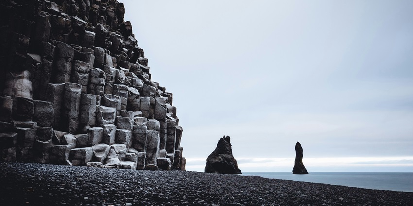 An image of Vik's black sand beach in Iceland, featuring ocean waves and cliffs.