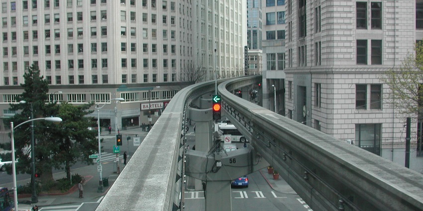 An elevated monorail bridge in Seattle with large tall buildings surrounding the bridge