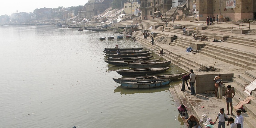 Morning mist over the Ganges River at Varanasi's ghats, with boats docked along the steps.
