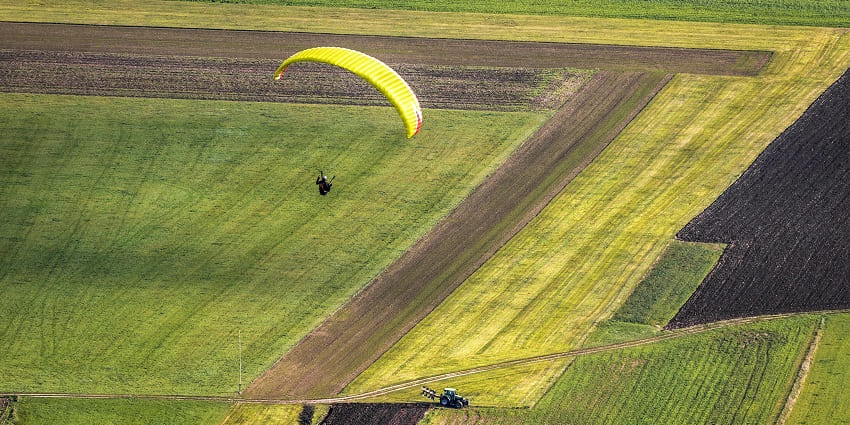 A man paragliding above green grasslands at a top spot for paragliding in Gurgaon