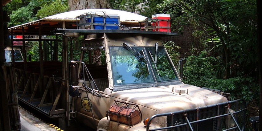 Empty safari vehicle parked in a very narrow space under a tree and greenery on a side.