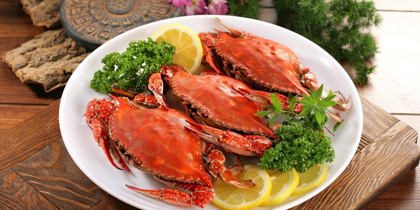 Seafood platter with crabs served with lemon slices and fresh leaves on a white plate.