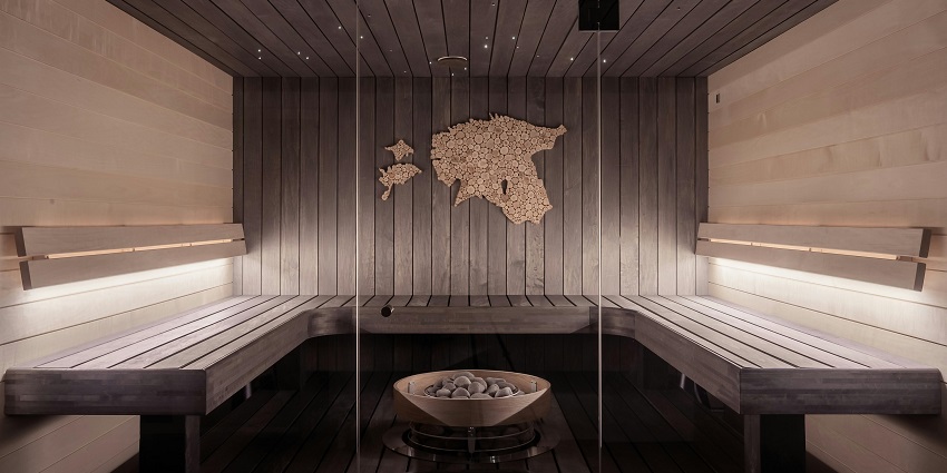 Inside a sauna with a glass door, sauna seats, a bowl full of stones and wall art