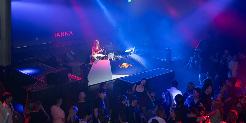 An image of a DJ playing music at a nightclub, with colourful lights and an energetic crowd
