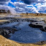 An image showing a group of people gathered near a steaming hot spring in a scenic location.