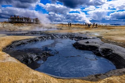 An image showing a group of people gathered near a steaming hot spring in a scenic location.