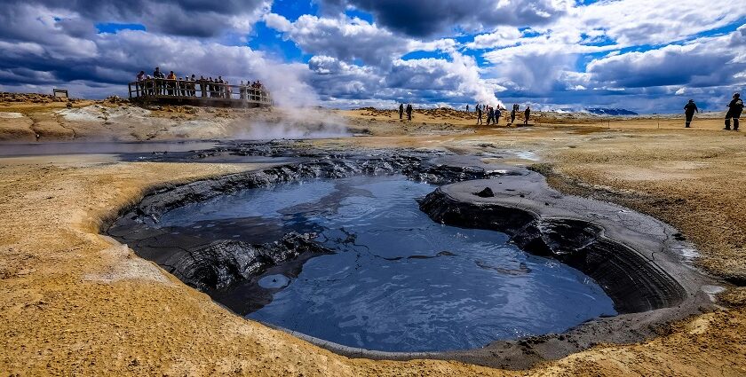 An image showing a group of people gathered near a steaming hot spring in a scenic location.