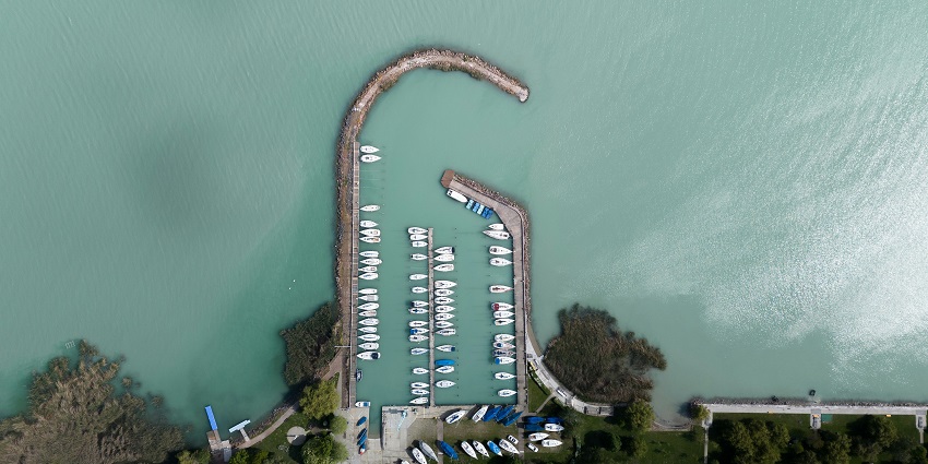 A serene sunset view of Lake Balaton, with folks along the waterfront and sailing boats.