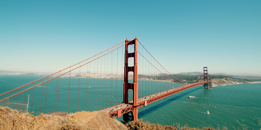 A large bridge spanning across a water reservoir with a mountain range in the backdrop