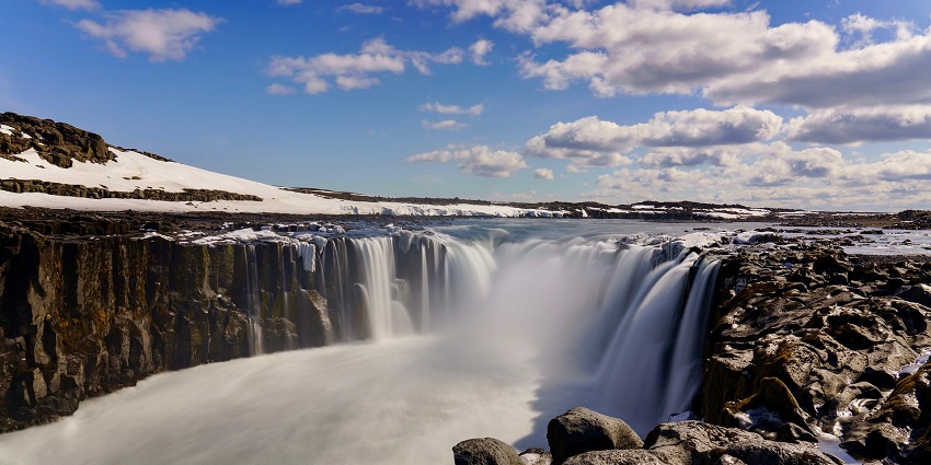 An image of the Selfoss waterfall, where powerful waters cascade over rocky cliffs, under a cloudy sky.