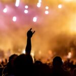 Crowd at a concert enjoying music with vibrant stage lights in the background.