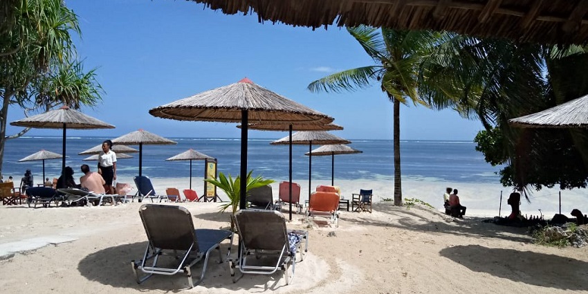People are enjoying their day on the beach chair under the umbrella at Shanzu Beach