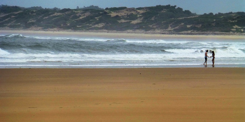 A couple is standing on Shela Beach and in the distance there are several small hills