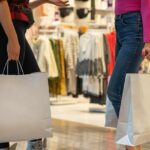 Two people standing and holding shopping bags and one person also carrying a backpack.