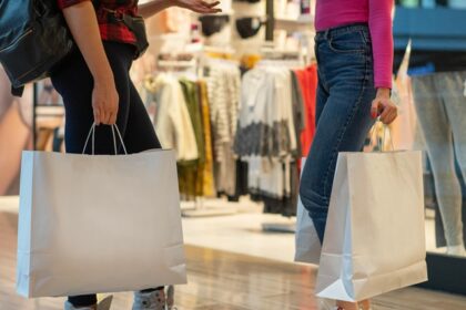 Two people standing and holding shopping bags and one person also carrying a backpack.