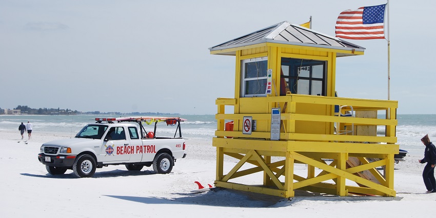 A long stretch of white sands with the sea at far is moderately crowded during sunset