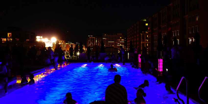 People swimming in the bright swimming pool with other people standing and passing by