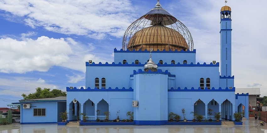 A man sitting on his knees on a red carpet in an old mosque and a light bulb hanging.