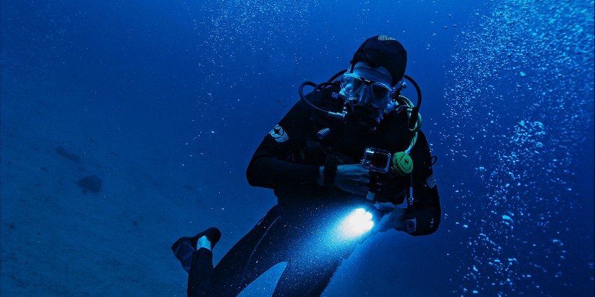 A scuba diver with an oxygen supply and diving gear holding a torch for clear vision