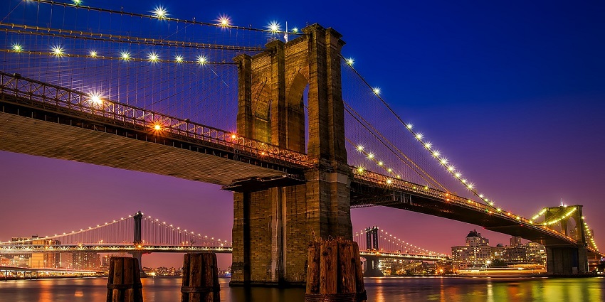 An image of a night view of illuminated buildings and a bridge with traffic on the river.