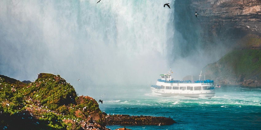 A cruise ship standing near the cascading waterfall and a rock covered with greenery