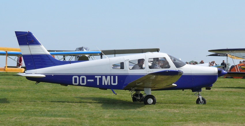 A Piper PA-28-161 Warrior II aircraft, registration OO-TMU, parked on a grassy airfield.