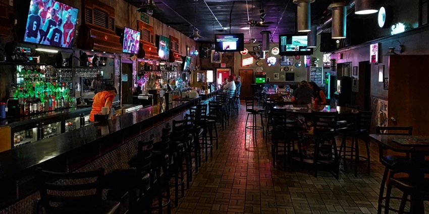 Bar with multiple televisions hanging, people sitting on the chairs and a bartender