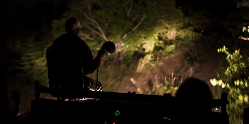 A man sitting in the front of the car holding a torch while another person driving the car