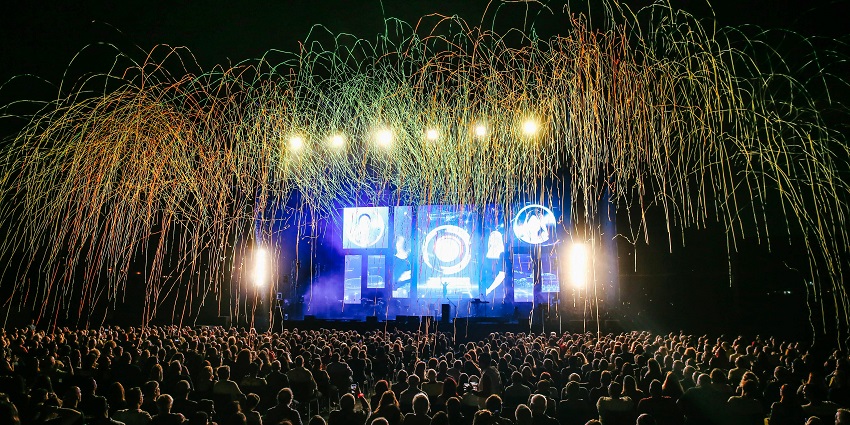 A crowd watching a live concert under stage lights, enjoying the music in an open-air setting.