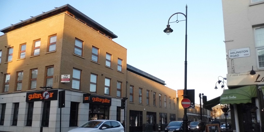 A view of Delancey Street at Arlington Road junction, featuring urban architecture and streetlights.
