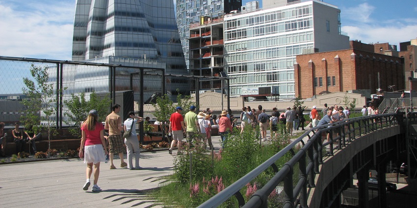 The image of people walking in the park with greenery and city buildings in the background.