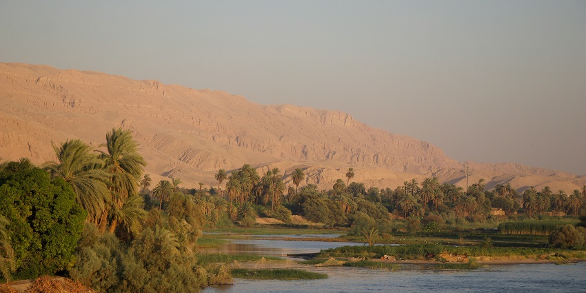 A small part of the Nile River body is surrounded by green xerophytes and sand dunes.