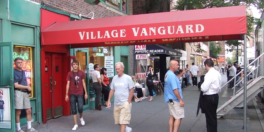 The Village Vanguard jazz club with a cosy, dimly lit interior, small stage, and intimate seating.