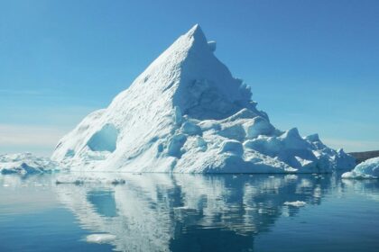 A clear reflection of a massive iceberg can be seen on the calm waters in Greenland.